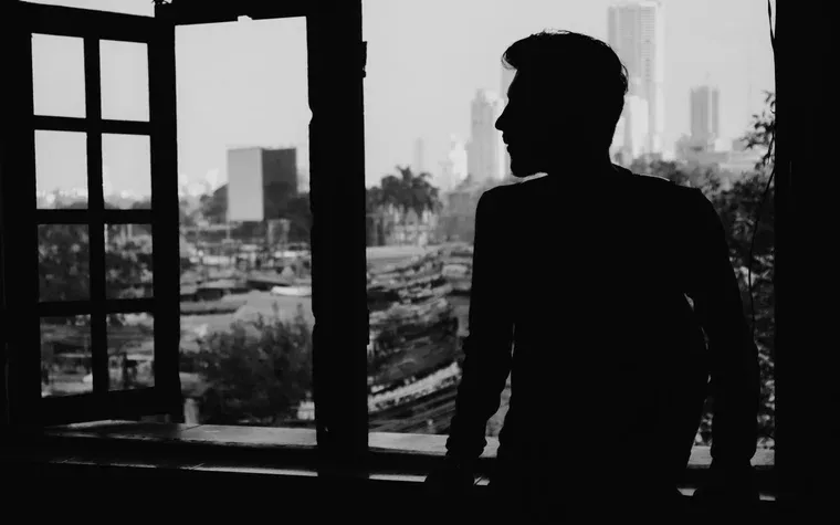 Silhouetted figure at an open window above a city